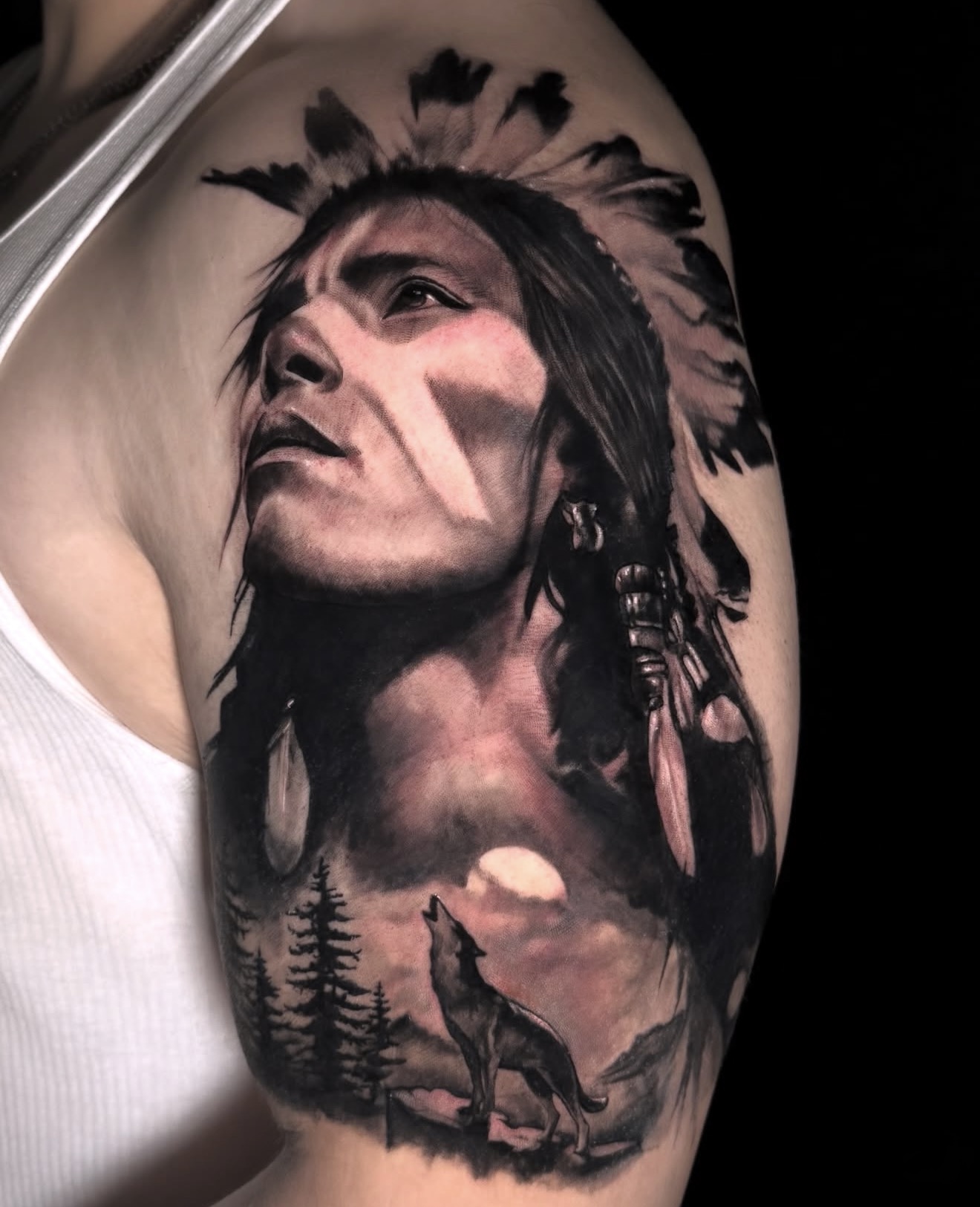 Native American portrait tattoo with feathered headdress wolf and landscape on upper arm